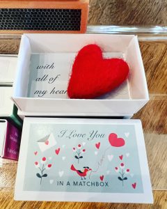 A small box with "I Love You in a Matchbox" on the lid, containing a red felt heart and a card reading "with all of my heart.