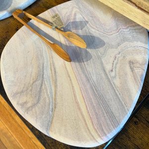 Round stone serving board with natural striations, wooden tongs resting on top, on a wooden table.