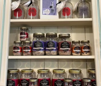 Shelves display assorted jars of drink mixes, including orange hibiscus, blueberry lavender, and raspberry mojito flavors.