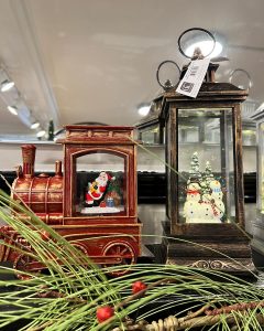 A Santa figurine in a train and snowmen in a lantern, with pine and berries in the foreground.