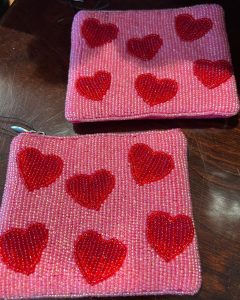 Two small pink zip pouches decorated with red beaded heart patterns on a dark wooden surface.