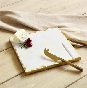 A marble cheese board with a gold-edged knife, a wedge of blue cheese, cranberries, and rosemary on a wooden table.