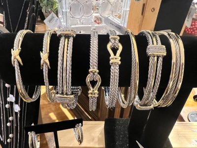 A display of silver and gold bracelets with various textures and designs arranged on a black velvet stand.