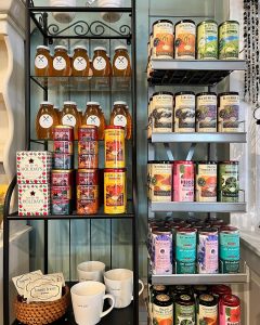 Shelves display assorted teas, honey jars, mugs, and holiday-themed gift items in a shop setting.