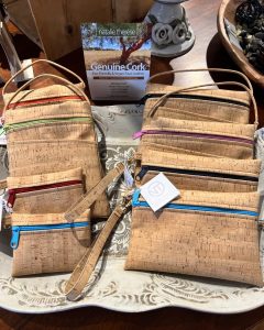 Several cork wristlet bags with colorful zippers are displayed on a decorative tray with a "Genuine Cork" sign behind them.
