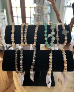 A black velvet display stand holds various beaded bracelets in neutral and turquoise tones, inside a well-lit shop.