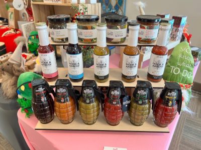 Various bottles of sauces and relishes, some shaped like grenades, displayed on a table in a store.