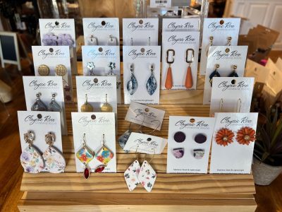 A display stand with assorted Classic Rose earrings, including floral, geometric, and drop designs on branded cards.