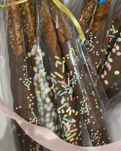 Chocolate-covered pretzel rods with colorful sprinkles, wrapped in clear plastic and tied with ribbons.