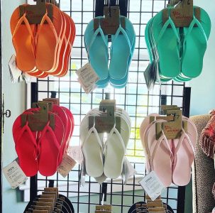 Colorful flip-flops in orange, blue, green, red, white, and pink hang on a metal display rack near a window.