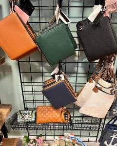 Assorted handbags and wallets in various colors displayed on a black metal rack in a retail store.