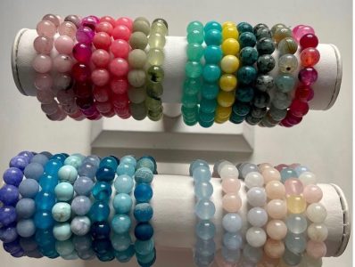 Two rows of colorful beaded gemstone bracelets displayed on a white stand, organized by color.