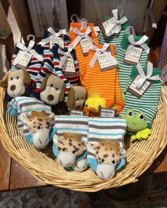 A wicker basket filled with striped baby socks featuring animal faces, including dogs, giraffes, a duck, and a frog.