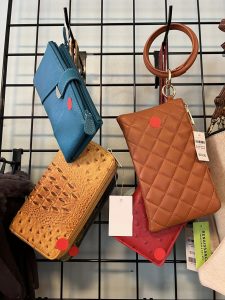Four small purses in different colors and textures are displayed on a black grid rack, each marked with a red sticker.