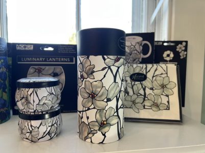 Three floral-patterned containers and matching napkins displayed on a shelf with packaged items in the background.
