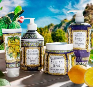 Four Sicilian Lemon skincare products are arranged on a table outdoors with cactus plants and mountains in the background.