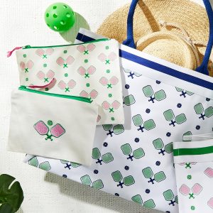 A tote bag, pouches, towel, straw hat, and green ball arranged on a light surface, all featuring a paddle design.