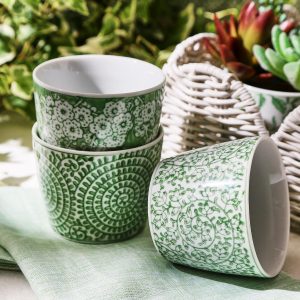 Three green and white patterned ceramic bowls are stacked, with one bowl lying on its side next to a woven basket with succulents.