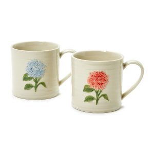 Two cream-colored mugs with molded handles, each featuring a raised floral design—one blue, one pink—on the side.