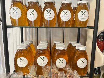 Jars of honey labeled “Nicker's Farm” arranged on glass shelves, with bags of pecans displayed below them.