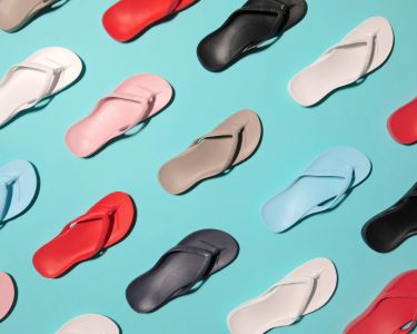 Various colored flip-flops are arranged in a diagonal pattern on a light blue background.