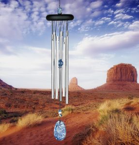 Wind chime with silver tubes and blue stones hanging in front of a desert landscape with mesas and cloudy sky.