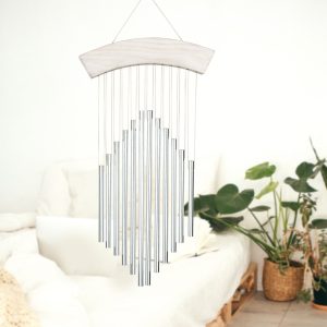 Silver metal wind chime with a wooden top hanging indoors near a bed and potted plants.