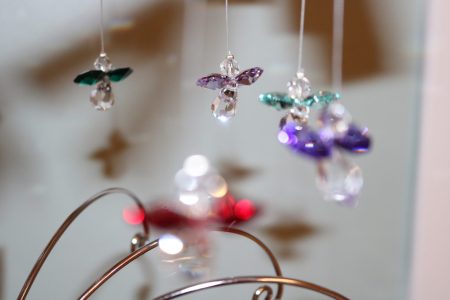 Close-up of crystal angel ornaments with colored wings hanging from thin threads, some in focus and others blurred.