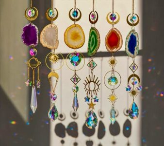Assorted crystal and gemstone sun catchers with gold accents hang in sunlight, casting colorful reflections and shadows.