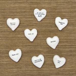 Eight white ceramic hearts with different messages are arranged on a textured brown surface.