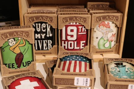 Assorted boxed flasks with various colorful designs and slogans are displayed on shelves in a store.