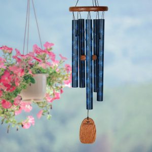 Blue wind chimes with a wooden clapper hanging outdoors near a pot of pink flowers.