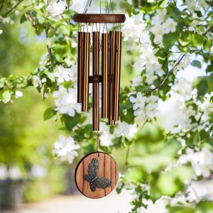 Wooden wind chime with metal tubes and a butterfly medallion hanging among white blooms on a tree branch.