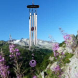 Silver wind chime with purple accents hanging outdoors, with mountains and purple flowers in the background.