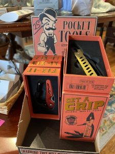 Display of pocket tools in orange boxes, including a red multitool knife and a yellow-handled pliers multitool.