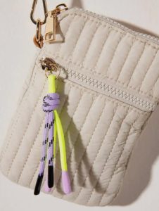 A quilted beige pouch with a zipper, keychain clip, and a decorative yellow and purple cord attached.