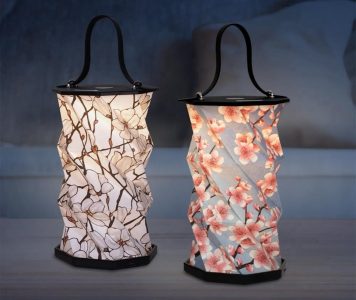 Two decorative lanterns with floral patterns and black handles, illuminated on a table in a dimly lit room.