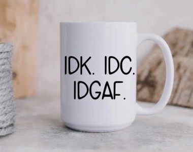White mug on a table with bold black text reading "IDK. IDC. IDGAF.