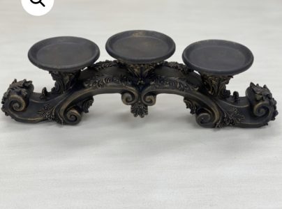 Ornate, antique-style metal candle holder with three round platforms and decorative scrollwork on a light background.