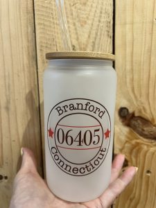 A hand holds a frosted glass jar with a straw and a lid, labeled "Branford Connecticut 06405.