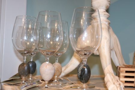 Four empty wine glasses with stones attached to their stems are arranged on a table next to a white decorative object.