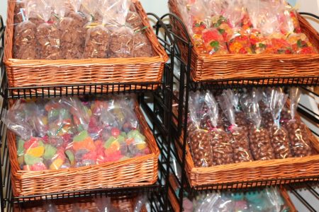 Wicker baskets filled with assorted bagged candies, including gummies and chocolates, displayed on black metal shelves.