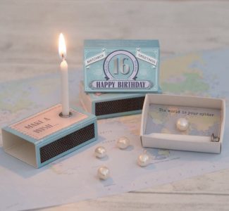 A lit birthday candle on a matchbox, a card reading "16 Happy Birthday," pearls, and a message: "The world is your oyster.