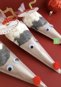 Three cone-shaped bags filled with hot cocoa mix, marshmallows, chocolate chips, googly eyes, and red pom-poms as noses.