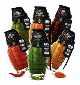 Five grenade-shaped bottles of The General’s Hot Sauce in various colors and flavors, arranged with assorted chili peppers.