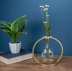A potted plant and a glass vase with white flowers sit on a wooden table against a blue wall.