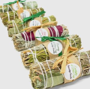 Five sage smudge bundles wrapped with string and labeled, arranged in a diagonal row on a white background.