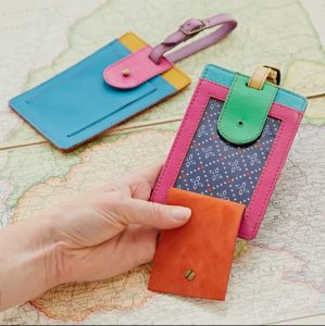 Two colorful leather luggage tags, one held by a hand, are displayed on a vintage map background.