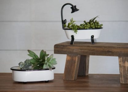 Two miniature bathtub planters with succulents, one on a wooden stool and one on a wooden surface.