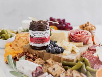 A charcuterie board with meats, cheeses, fruits, crackers, and a jar of Terrapin Ridge Farms hot pepper bacon jam.